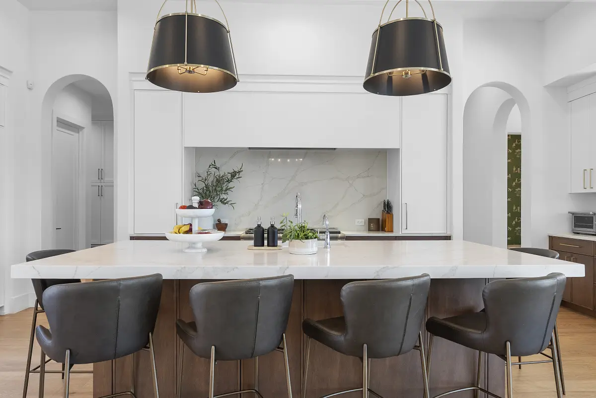 White kitchen with black drum pendants and a marble backsplash